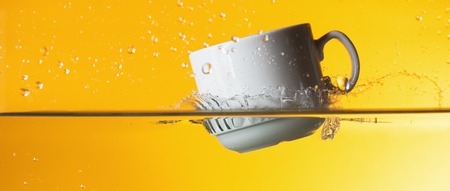 Coffee cup in water splash over yellow backgroundの写真素材