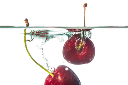 Closeup of cherries falling in water, isolated on white backgroundの写真素材