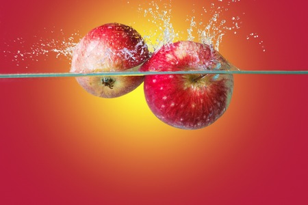 Apples falling in water over bright yellow-red backgroundの写真素材