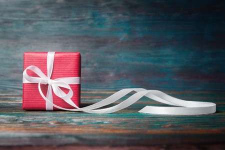 Red gift box with long ribbon over blur wooden background