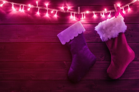 Two Santa socks hanging on glowing garland over woodenの写真素材