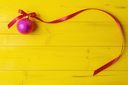 Pink Christmas ball with long curly ribbon on yellowの写真素材