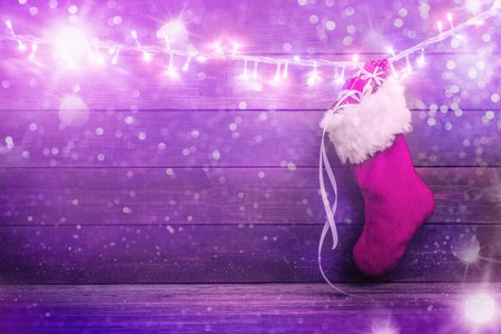 Pink Santa stocking with gift boxes hanging on glowing garland over holiday woodenの写真素材