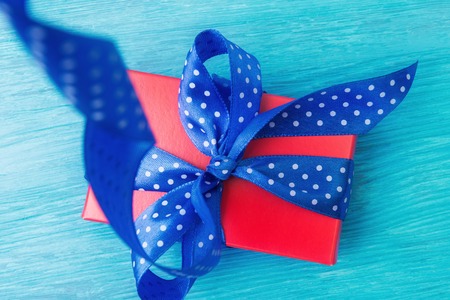 Close up of red gift box with spotted blue bow over woodenの写真素材