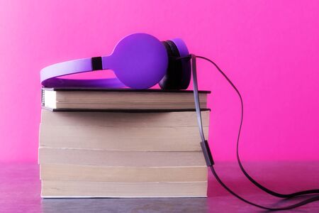 Stack of books and headphones over pink
