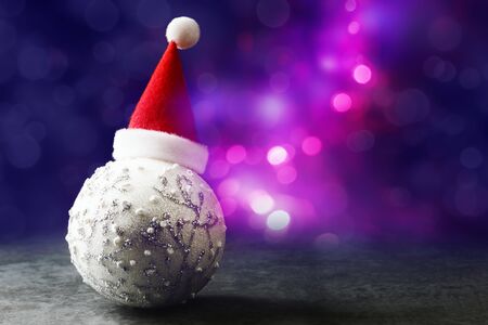 Xmas bauble in red Santa hat over defocused Christmas lights.の写真素材