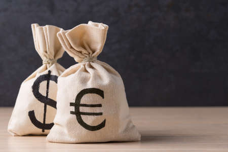 Money bags with USD and Euro symbols on dark background with copy space. Selective focus on...