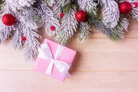 Pink gift box, Christmas decoration and frosty fir tree branches over wooden background with copy spaceの写真素材