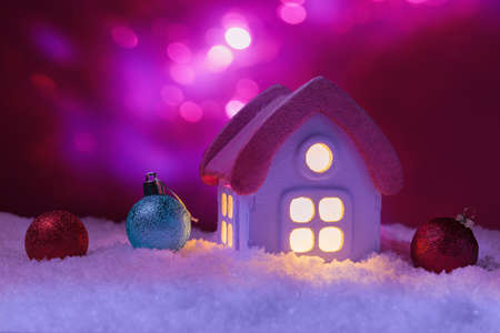 House in snow with glowing windows and Christmas decoration over holiday lights. Xmas and New Year...