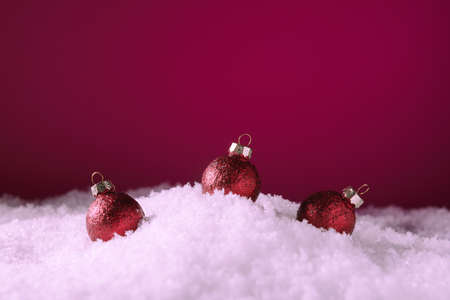 Three red Christmas baubles in snow over pink background with copy spaceの写真素材