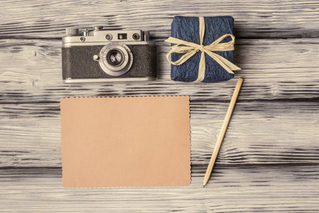 Vintage camera with blank card and gift box on old wooden background