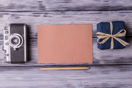 Flat lay of vintage camera with blank card and gift box on old wooden background