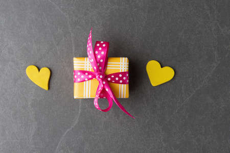 Two yellow hearts and gift box on grey stone background. Valentineâ€™s day trendy greeting