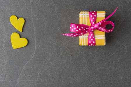 Gift box and yellow decorative hearts on grey stone background