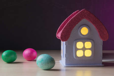 Toy house with glowing windows and painted Easter eggs over dark backgroundの写真素材