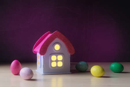 Toy house and decorative Easter eggs over dark violet backgroundの写真素材