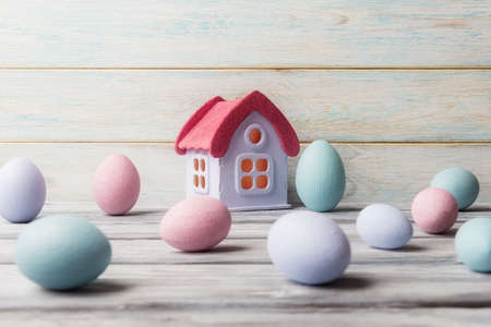 House model and colored Easter eggs over light wooden backgroundの写真素材