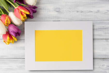 Tulip flowers and yellow blank card in white frame on wooden background