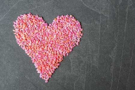 Valentine heart shape made of small pink and red rocks on grey stone background with copy space. Valentines day greeting conceptの写真素材