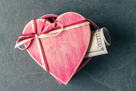 100 USD banknotes in heart shaped gift box on grey stone background. Love and money conceptの写真素材