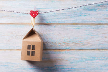 Craft toy house hanging on a rope over light wooden background with copy space. Valentines day greeting cartの写真素材