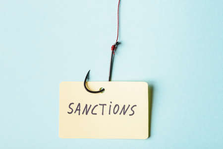 Paper card with word Sanctions on fish hook over blue background. Economic sanctions risk conceptの写真素材