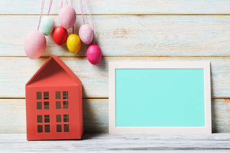 Easter still life with house model, decorative eggs and blank blue card with copy spaceの写真素材
