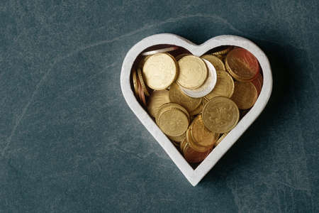 Euro coins in heart shaped white box on dark stone background with copy spaceの写真素材