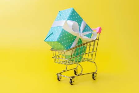 Shopping trolley with blue gift box over yellow backgroundの写真素材