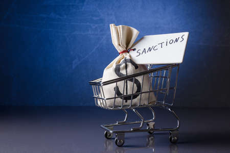 Money bag with label "Sanctions" in shopping cart over blue backgroundの写真素材