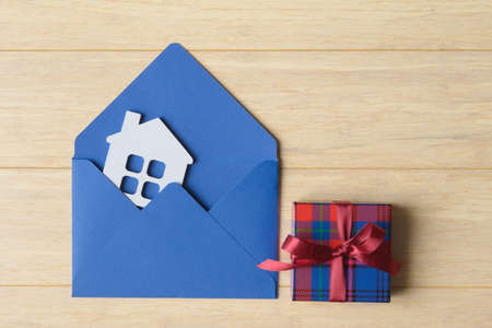 House model in blue envelope and gift box on wooden background. Mortgage and house buying conceptの写真素材