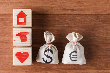 Moneybags with USD and Euro symbols and wooden cubes with icons of education, love and house. Concept of modern valuesの写真素材