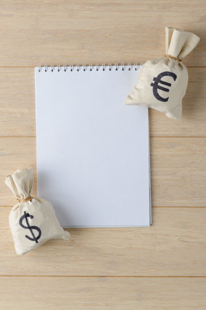 White blank notebook page and moneybags with USD and Euro on wooden background. Financial planning conceptの写真素材