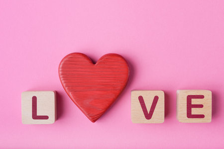 Red heart and wooden cubes with the word love on a pink backgroundの写真素材