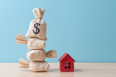 Money bags with Dollar sign and small red house model over blue background with copy space. Concept of house buying and mortgageの写真素材