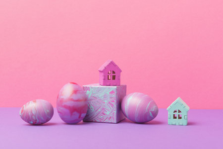 Decorative Easter eggs painted in fluid art technique and house model against pink background. Creative Easter holiday greeting conceptの写真素材