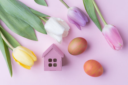 Tulip flowers, decorative Easter eggs and house model on pink background. Easter holiday greetingの写真素材