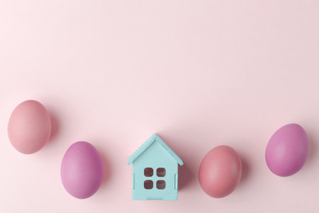House model and painted Easter eggs on light pastel background with copy spaceの写真素材