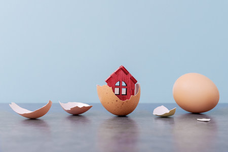 Tiny house in eggs shell over blue background with copy space. Conceptual Easter greeting cardの写真素材