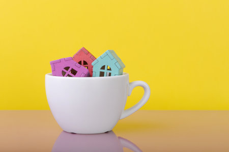 House models in coffee cup over yellow background with copy space. Home buying and mortgage concept. House sale proposalの写真素材