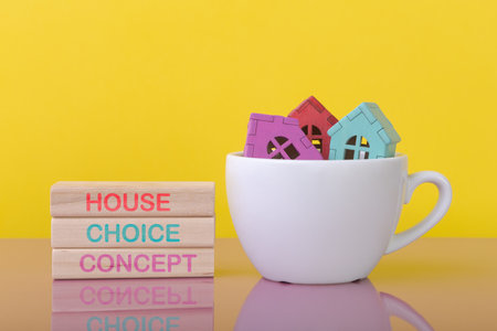 White cup with house models and wooden blocks with words House Choice Concept. Yellow background with copy space. House purchasing and mortgage conceptの写真素材