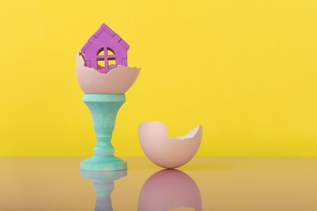 House model in eggshell over yellow background with copy space. Conceptual ad for house innovation...