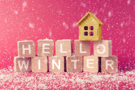 House model on wooden blocks with inscription Hello winter. Snowy background. Concept of real estate and mortgage in winter time and holidaysの写真素材
