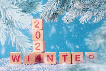 Wooden blocks with inscription 2024 winter and frosty Christmas tree branches. Blue snowy background with copy space. Concept of coming  winter holidaysの写真素材