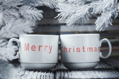 Two cups of hot coffee with words Merry Christmas and snow-covered fir branches. Christmas and New Year greeting conceptの写真素材