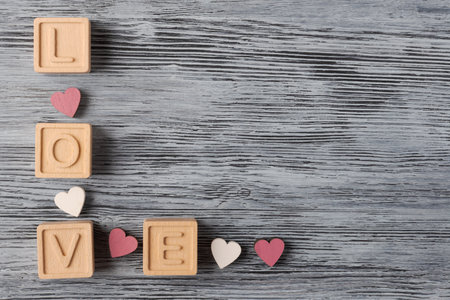 An image displaying the message âLOVEâ spelled out with wooden blocks and adorned with small red hearts on textured wooden background. Valentines day conceptの写真素材