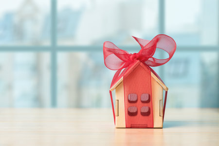 Small house gift with red bow over defocused cityscape with copy space. Concept of real estate gift or purchasingの写真素材