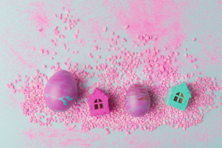 Easter holiday composition with painted eggs in fluid art technique and houses on small pink stones....