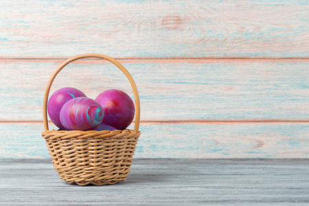 A wicker basket filled with vibrant, hand-painted Easter eggs against a rustic wooden backdrop with copy spaceの写真素材