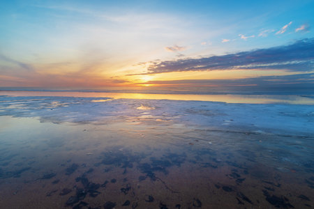 A tranquil beach scene capturing a breathtaking sunset in winter time. The skyâs warm hues reflect on calm waters and ice creating a serene atmosphereの写真素材